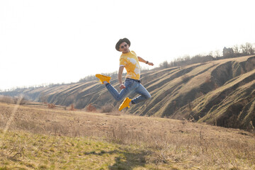 A young man jumping yellow t-shirt and white sneakers in spring mountains at sunset and enjoying view of nature. Mountain and coastal travel, freedom and active lifestyle