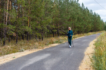 Obraz premium slender woman of retirement age is engaged in Nordic walking in the park