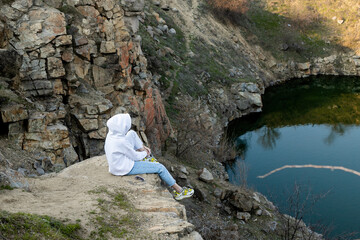 girl sits on the edge of a mountain in a white hoodie and looks at the lake, Mountains. Traveling