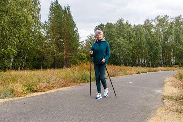 slender woman of retirement age is engaged in Nordic walking in the park