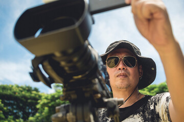 An asian male videographer using a professional camcorder mounted on a tripod. Documenting an...