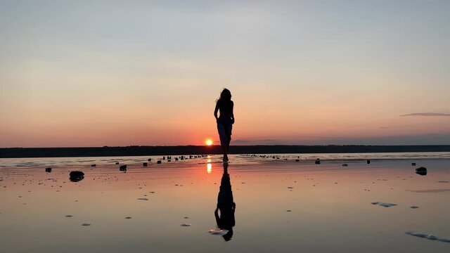Silhouette of a beautiful woman dancing in the background of the sunset in the water. Ballet, dance, improvisation of contemporary dance.