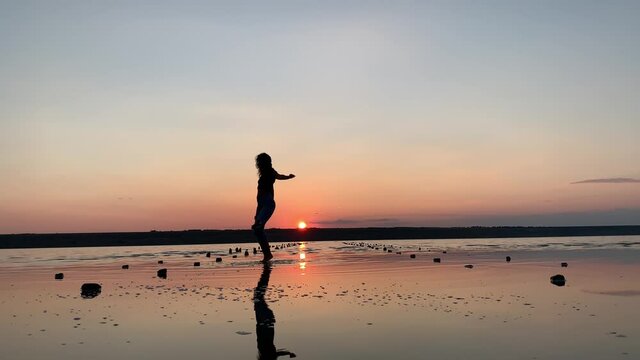 Silhouette of a beautiful woman dancing in the background of the sunset in the water. Ballet, dance, improvisation of contemporary dance.