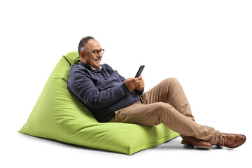 Mature man sitting on a green bean bag chair and using a mobile phone