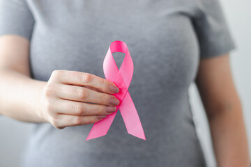 Woman in gray t-shirt holds pink ribbon in her hands. Breast Cancer Awareness Month. Supporting and promoting campaign against cancer.