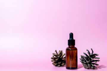 Obraz na płótnie Canvas Brown glass serum bottle with pipette and pine cone on pink background with copy space. Body care serum cosmetic skin care. Front view with copy space.