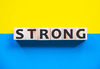 Word STRONG on wooden cubes with word on beautiful yellow and blue background. Business, media marketing concept.