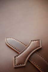 Leather clasp in the shape of a cross close-up on smooth brown leather. Leather goods, handmade work, backgrounds concept.