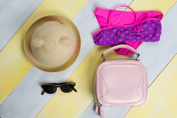 on a gray-yellow surface, a children's swimsuit, sunglasses, a hat and a purse