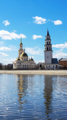 Leaning Tower of Nevyansk and Old Believers' church (domed) in spring day on the shore of the pond in Sverdlovsk Oblast, Russia. Vertical shot