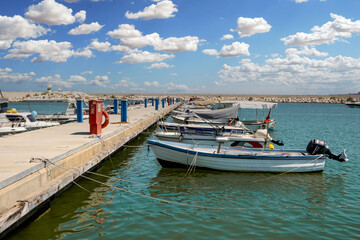 Row of small boats tied to a dock in a harbor. Cloudy blue sky