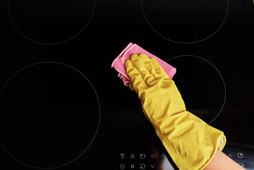 Cleaning induction stove. Woman in yellow rubber gloves cleans kitchen induction hob with cleaning...