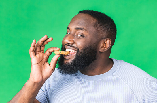 Portrait of young african american black man holding chocolate cookie biscuit isolated on green background.