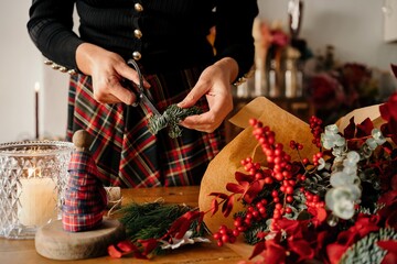 Florist making Christmas bouquet on wooden table in daylight