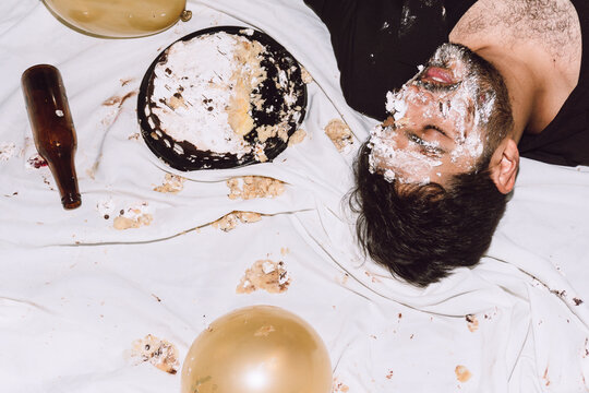 Drunk man lying on messy cloth with smashed cake