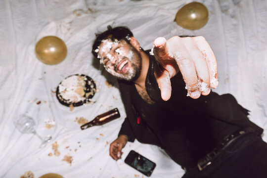 Happy man in smashed cake pointing at camera