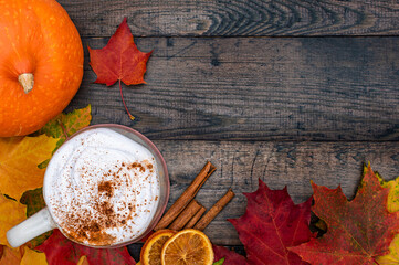 Colourful autumnal maple leaves border with cup of spiced coffee and pumpkin. Natural yellow, orange and red maple leaves. Cappuccino with cinnamon and dried oranges on wooden table with copy space.