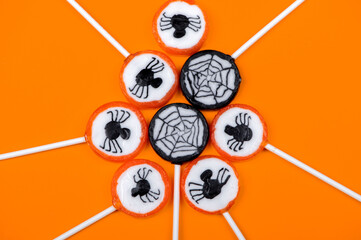 Halloween candy with black spiders and cobweb on orange color background,top view
