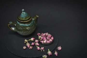 Dried tea rose buds and ceramic vintage teapot for tea ceremony in chinese style on black background.