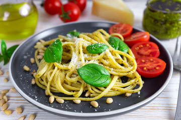 Traditional italian pasta with fresh vegetables, parmesan cheese, basil leaves, pine nuts and pesto sauce in black plate on white wooden background.