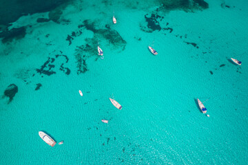 Fototapeta na wymiar Aerial view of many yachts and sailboats in turquoise water in Mediterranean Sea next to Sardinia island, La Pelosa beach