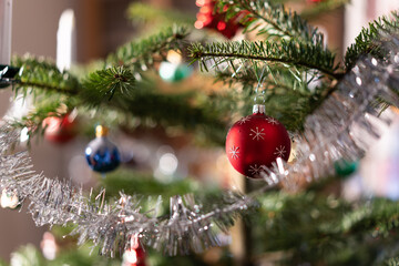 Close-up of a branch of Christmas tree with wreath, tinsel and colorful baubles indoor at daytime.
