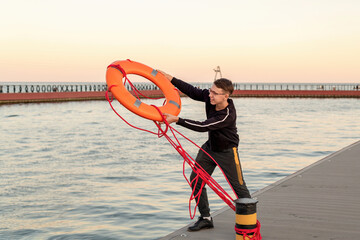 A guy on a pier near the sea throws an orange life buoy into the sea.