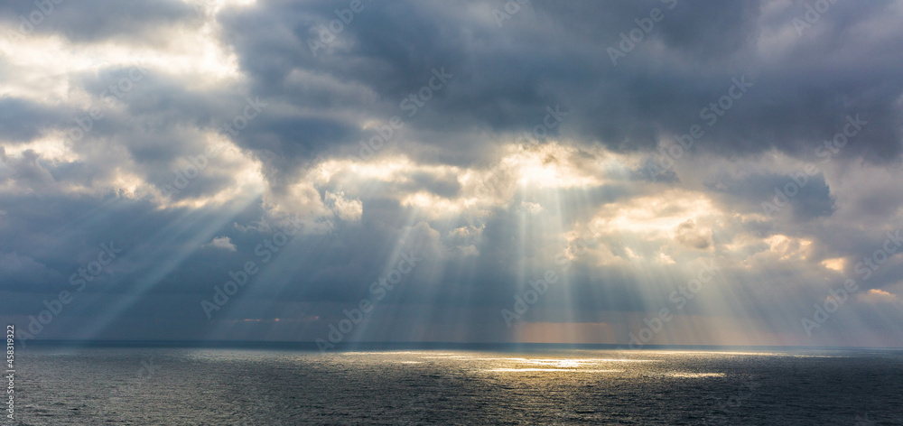 Wall mural The sun breaks through the clouds illuminating the sea with its rays. 