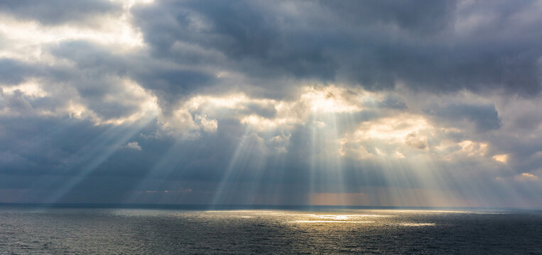 The sun breaks through the clouds illuminating the sea with its rays. 