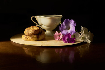 An appetizing homemade bun with a cup of tea and a bouquet of flowers. Dark background. Free space for text.