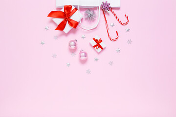 Christmas, New Year composition. White paper bag with presents, sweet candy canes, holiday decorations, pink balls, silver glitter confetti stars on pastel pink background. Flat lay, copy space.