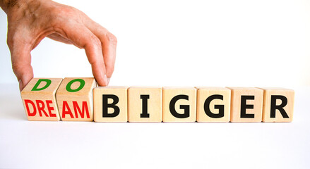 Dream and do bigger symbol. Businessman turns wooden cubes and changes words dream bigger to do bigger. Business and dream and do bigger concept. Beautiful white background, copy space.