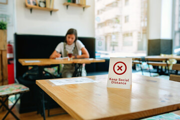 Coffee shop table with do not use sign to keep social distance with girl in the background having a drink