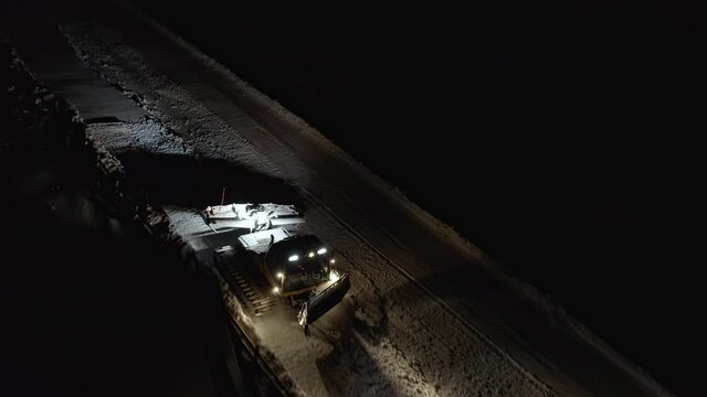 Snow grooming machine on a ski slope at night. View from above