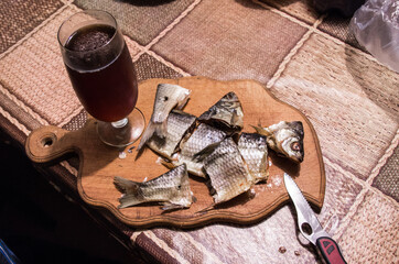 A glass of beer and sliced fish. Sliced dried fish on a wooden board. Drink beer at home.