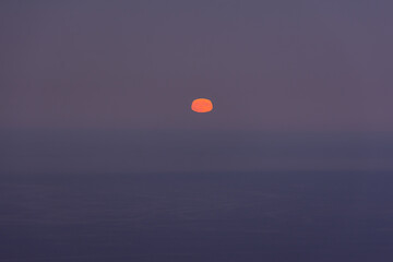 Full moon sea. The supermoon is orange in a purple sky over the ocean. Horizontal minimalistic natural night background. A mystical landscape with a rising yellow moon. Mysterious Halloween background