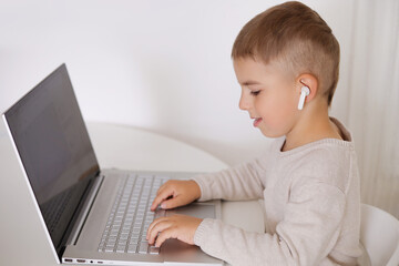 Happy little boy playing game on laptop at home. Portrait of a child at home watching cartoon on the computer. Modern kid and education technology.