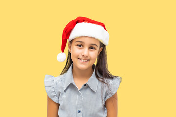 Portrait of pretty christmas girl in white dress and santa hat, smiling isolated on yellow background
