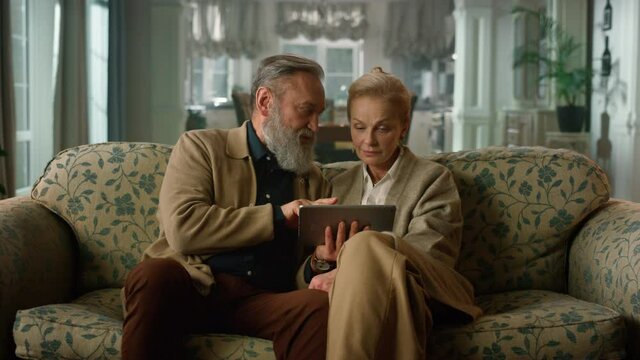 Charming mature couple surfing internet on digital device at luxury home.