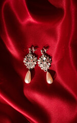 Women's earrings on red silk background. Round golden earrings with brilliant gemstones, close-up. Elegant woman jewelry, selective focus