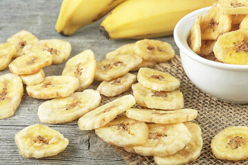 Dried banana slices and fresh bananas on wooden table. Banana chips. Banana dessert.