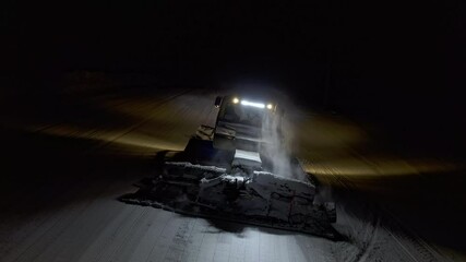 Snow grooming machine on a ski slope at night. View from above