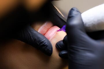 the permanent makeup artist performs the first pass of applying lip pigment