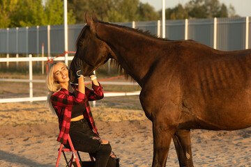Young woman farmer in a red checkered shirt hugs her horse concept of love between people and animals.