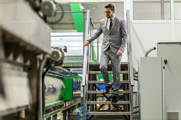 Angry businessman in a factory. The disgruntled manager in elegant suit quickly descends the stairs at the production factory. Low business results and frustrations due to poor management