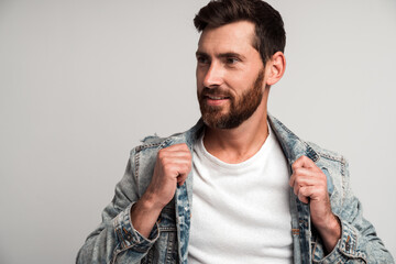 Portrait of bearded handsome man in casual style looking away and smiling while straightening his...