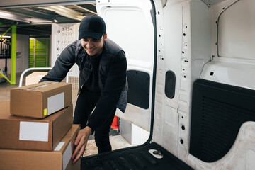 Smiling male courier working in warehouse upload boxes into a van for delivery © Artem Varnitsin