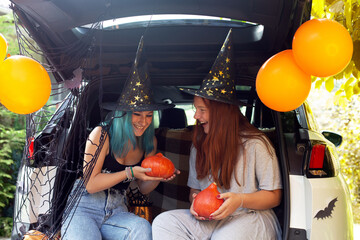 Two girls generation Z celebrating Halloween car trunk. Autumn holidays