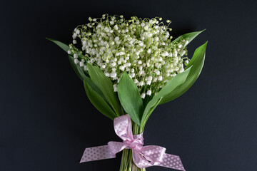 Happy holiday concept. A bouquet of beautiful fragrant white lilies of the valley on a dark background.