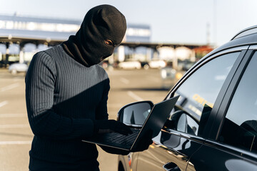 Waist up portrait of the car thief with laptop hacking alarm system while standing near the car at the daytime. Stock photo